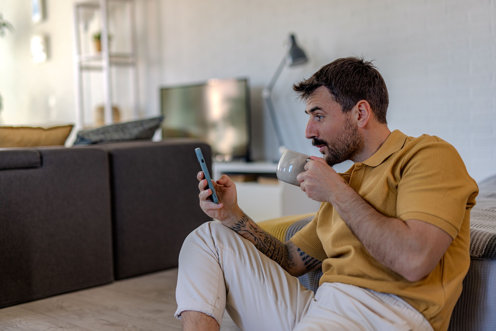 Man drinking coffee and using smartphone at home